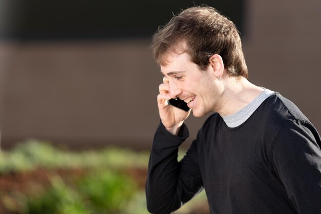 Nahaufnahmeporträt eines glücklichen jungen Mannes, der gute Nachrichten erhält, während er draußen am Telefon spricht.