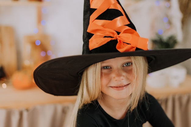 Nahaufnahmeporträt eines kleinen blonden Mädchens mit blauen Augen in einem schwarzen Hut und einem schwarzen Halloween-Pullover