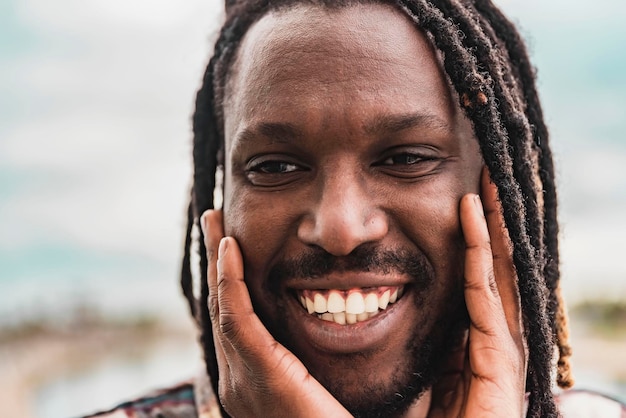 Nahaufnahmeporträt eines lächelnden afroamerikanischen Mannes mit seinen Händen auf seinem Gesicht