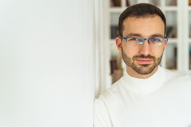 Nahaufnahmeporträt eines ruhigen, gutaussehenden jungen Mannes in stilvollen Brillen, die sich an die Wand lehnen