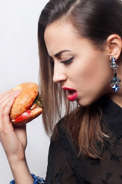 Nahaufnahmeporträt eines schönen brünetten Mädchens, das einen großen Hamburger isst