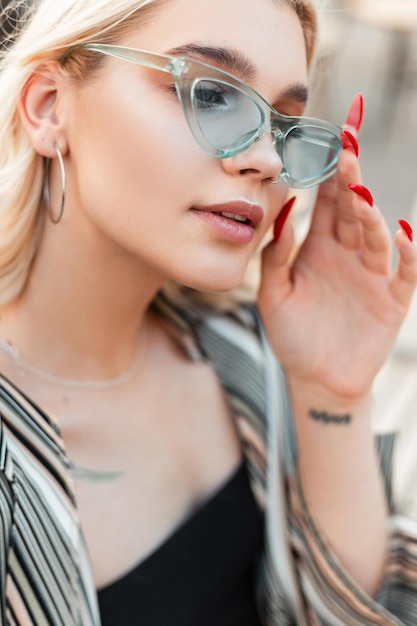 Nahaufnahmeporträt eines schönen jungen Mädchenmodells in modischer blauer Sonnenbrille mit lässigem Sommeroutfit in der Stadt