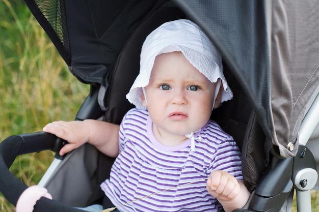 Nahaufnahmeporträt eines süßen Kleinkindmädchens in einem weißen Panamahut, das im Sommer in einem Kinderwagen sitzt