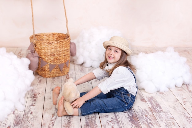 Nahaufnahmeporträt Nettes lächelndes kleines Mädchen, das auf Wand eines Ballons, der Sterne und der Wolken sitzt und einen Teddybär hält. kleines Mädchen träumt. Mädchen spielt im Kinderzimmer mit einem Spielzeug. Kindheit