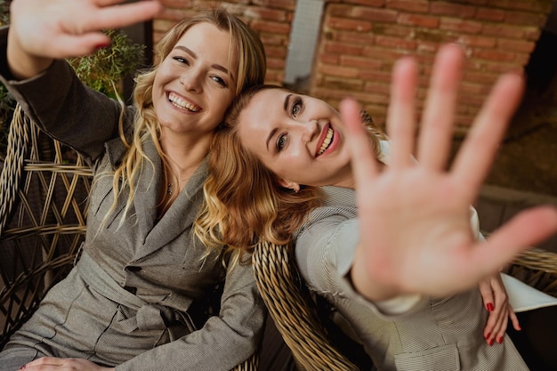 Nahaufnahmeporträt von zwei Freundinnen in strengen grauen Anzügen, die lachen und Gesichter mit den Händen schließen