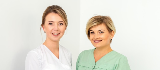 Nahaufnahmeporträt von zwei jungen lächelnden weiblichen kaukasischen Beschäftigten im Gesundheitswesen, die auf weißem Hintergrund in die Kamera starren