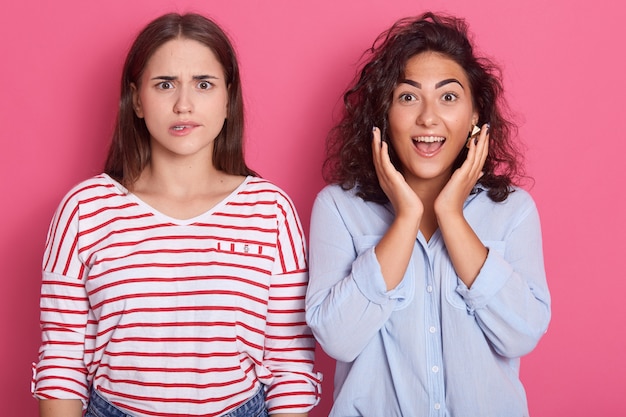 Foto nahaufnahmeporträt von zwei verblüfften jungen frauen, die eng beieinander stehen und mit abgehörten augen starren