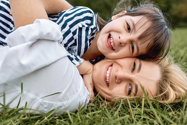 Nahaufnahmeportrait der hübschen Frau, die mit ihrem niedlichen kleinen Mädchen auf grünem Gras im Freien spielt Liebevolle hübsche Tochter, die lächelt und ihre schöne Mutter umarmt Glückliche Mutterschaft Kindheit Muttertag