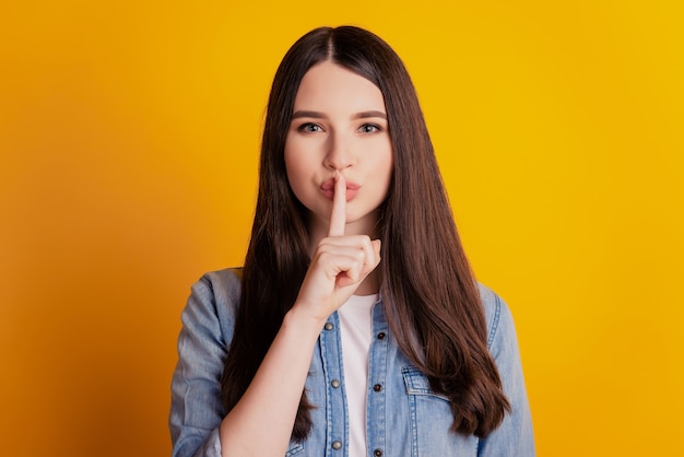 Nahaufnahmeportrait der schlauen Frau, die Finger bedeckt, die Lippen lokalisierten gelben Wandhintergrund