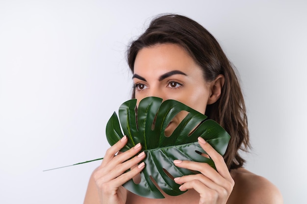 Nahaufnahmeschönheitsporträt einer schulterfreien Frau mit perfekter Haut und natürlichem Make-up mit Monstera-Palmblatt