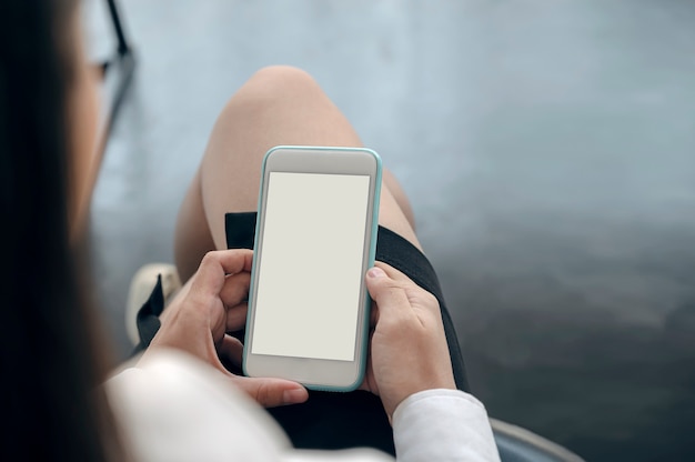 Nahaufnahmeschuss der Frauenhand, die Smartphone des leeren Bildschirms beim Sitzen im Büro hält.