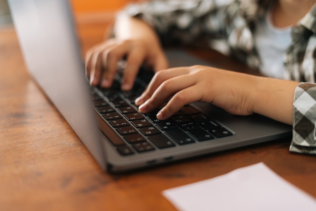 Nahaufnahmeseitenansichthände von nicht erkennbarem Grundschulmädchen, das auf Laptoptastatur tippt