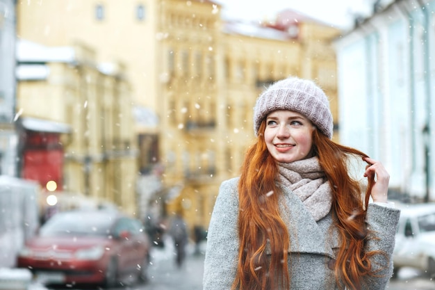 Nahaufnahmestraßenporträt einer eleganten rothaarigen Frau, die während des Schneefalls in der Altstadt spaziert. Freiraum