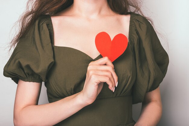 Nahes Porträt eines verliebten Mädchens, das ein Papierherz auf ihrer Brust hält