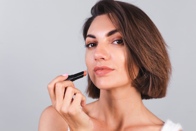 Nahes Schönheitsporträt der Frau mit Make-up und braunem Lippenstift auf grauer Wand