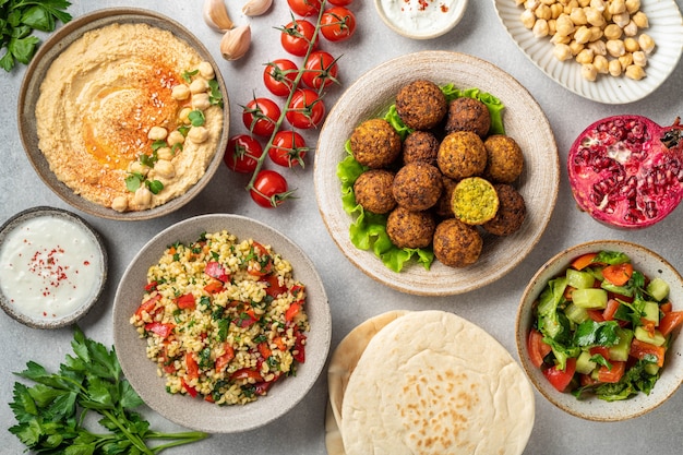 Nahöstliche oder arabische Küche, Falafel, Hummus, Tabouleh, Pita und Gemüse auf einem Betontisch, Ansicht von oben