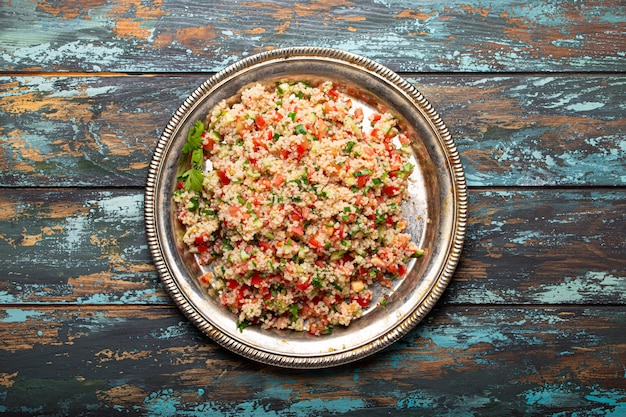 Nahöstliches und mediterranes traditionelles Gemüsesalat-Tabouleh mit Couscous auf rustikaler Metallplatte und Holzhintergrund von oben. Arabisches türkisches Essen