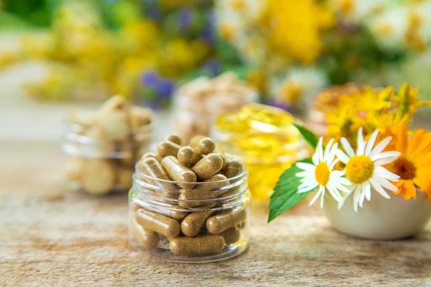 Nahrungsergänzungsmittel und Kräuter in einer Schüssel und Gläsern auf einem Holztisch mit unscharfem Blumenhintergrund