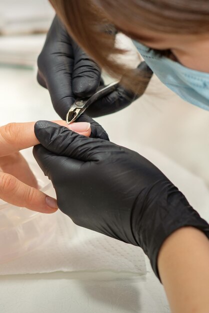 Nail master removendo a cutícula das unhas com uma pinça, higiene de manicure em um salão de beleza.