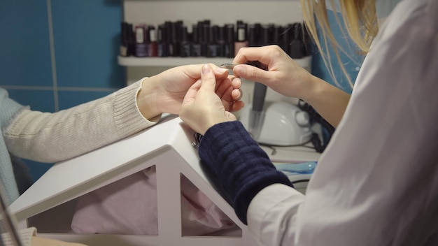 Nail master trata la cutícula de una joven clienta con unas pinzas de manicura en un salón de belleza.