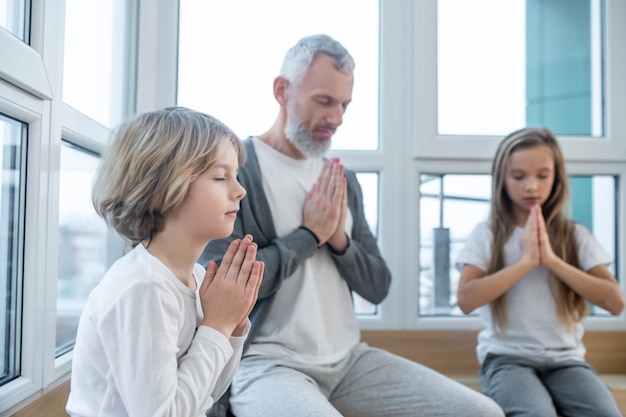 Namaste. Hombre canoso y sus hijos sentados pacíficamente con namaste