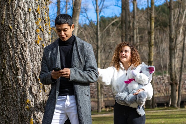 Namorada dando um ursinho de pelúcia para o namorado ao ar livre Jovem mulher dando um ursinho de pelúcia para o namorado em um dia especial