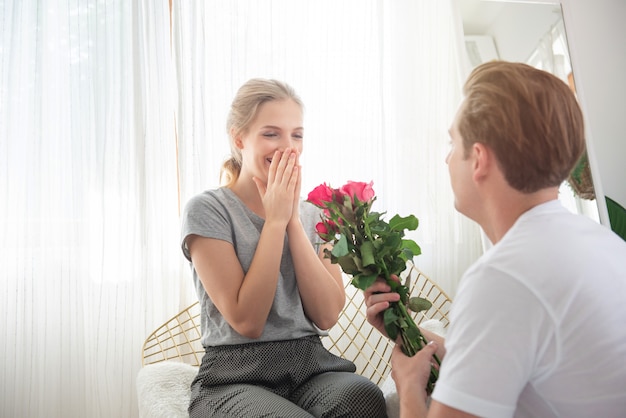 Namorada de surpresa jovem homem caucasiano com monte de rosa para comemorar seu aniversário de casamento day.couple tem tempo feliz juntos em casa. conceito de dia dos namorados.