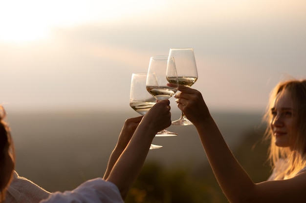 Foto namoradas fazem um brinde com taças de vinho branco em um pôr do sol