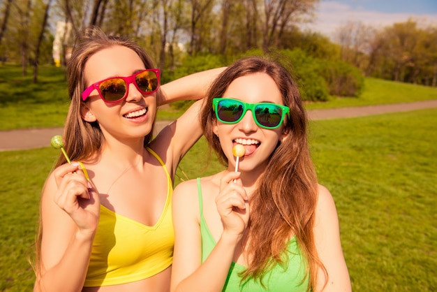 Namoradas felizes e alegres de óculos lambendo chupa chups