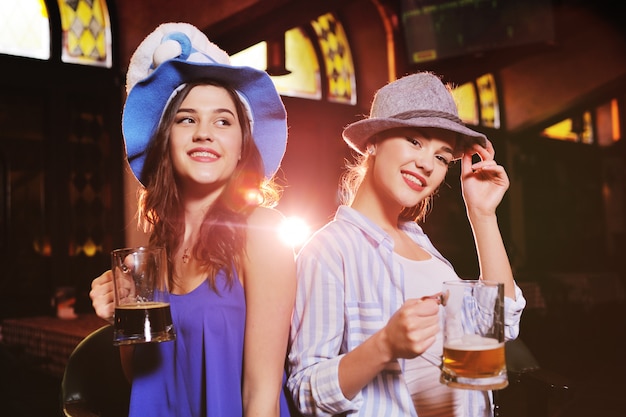 Namoradas jovens bonitos em chapéus da Baviera sorrindo no bar