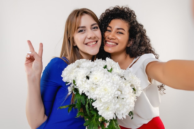 Foto namoradas multirraciais fazendo selfie com buquê de flores brancas isolado