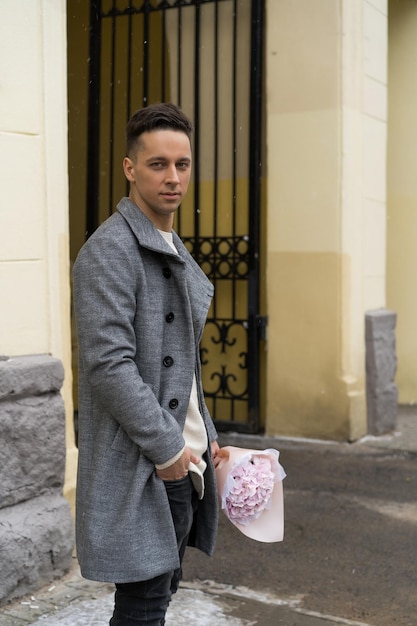 Namorado com um buquê de flores cor de rosa hortênsia esperando por sua namorada ao ar livre enquanto a neve está caindo. Conceito de dia dos namorados, proposta de casamento. homem vai a um encontro.