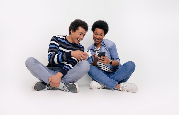 Foto namorado e namorada despreocupados lendo mensagens e rindo enquanto estão sentados sobre um fundo branco