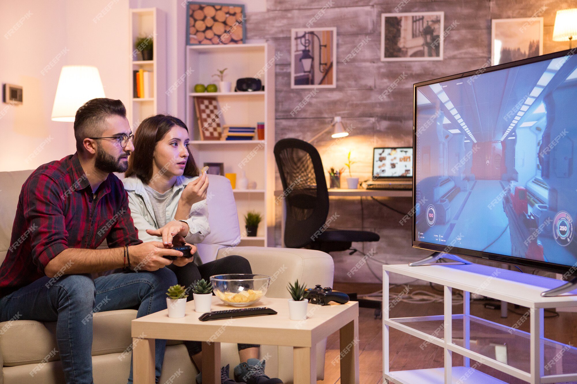 Jogador jogando videogame de console de tiro em primeira pessoa na tv  enquanto a namorada está comendo pipoca e dando-lhe conselhos sentado no  sofá. casal no sofá desfrutando de simulação de jogos