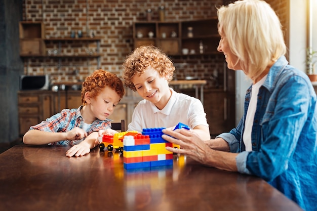 Não há lugar como o lar. Foco seletivo em irmãos de cabelos cacheados sorridentes brincando com blocos de construção e construindo carros