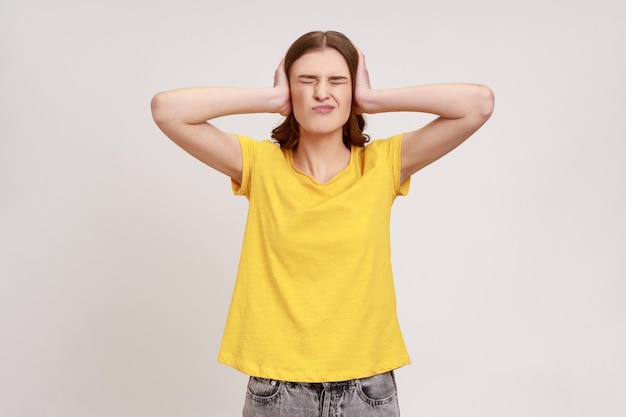 Não quero ouvir Linda jovem estressada irritada em roupas de estilo casual cobrindo os ouvidos mantendo os olhos fechados colapso nervoso Foto de estúdio interior isolada em fundo cinza