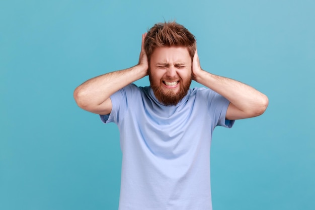 Não quero ouvir Retrato de homem desesperado irritado com barulho alto cobrindo os ouvidos e fazendo caretas de dor sofrendo som irritante de alto decibel Tiro de estúdio interno isolado em fundo azul