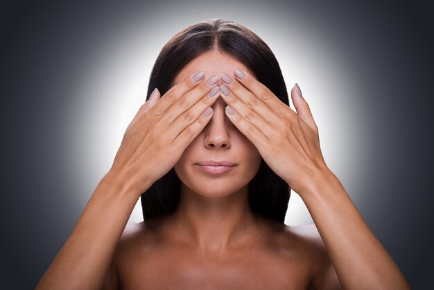 Foto não vejo nada! retrato de uma jovem mulher sem camisa, cobrindo os olhos com as mãos em pé contra um fundo cinza