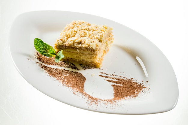 Napoleon-Kuchen mit Minzblatt auf Teller auf Weiß