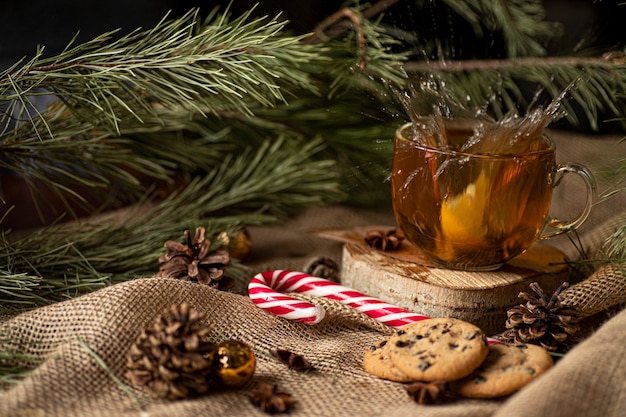 naranja cae en el té y salpica, junto a galletas y piruletas en un árbol de Navidad y conos.