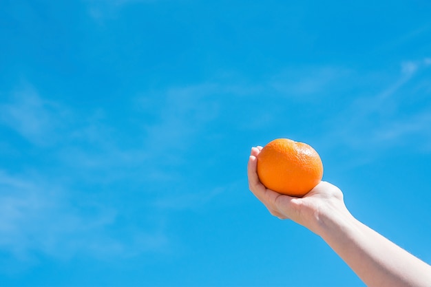 Naranja celebrada en mano sobre fondo de cielo azul.