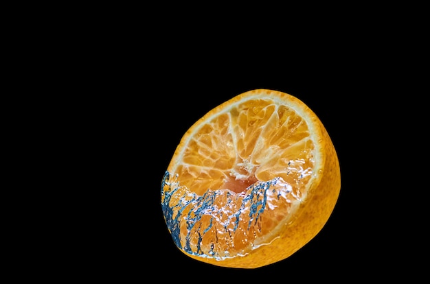 Naranja fresca que cae en el agua con salpicaduras sobre fondo negro