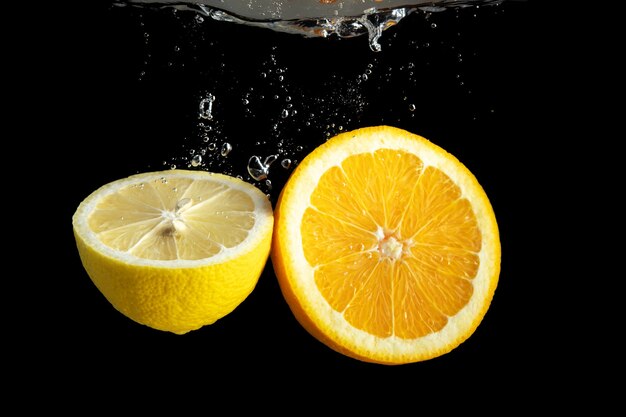 Naranja y limón en rodajas frescas en salpicaduras de agua aislado en negro.