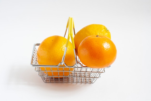 Naranja, mandarina y limón en una canasta de comestibles aislado en blanco