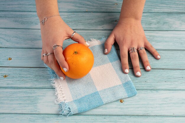 Naranja en manos sobre una mesa de madera azul