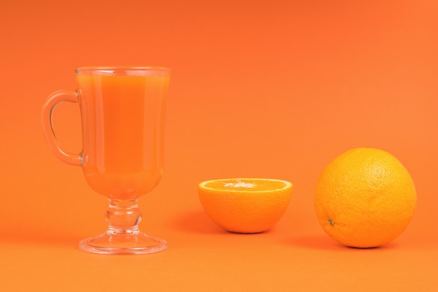 Una naranja en rodajas y un vaso de vidrio con un batido sobre un fondo naranja.