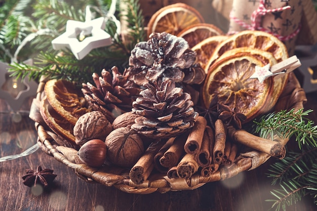 Naranja seca, anís estrellado, canela, piñas y abeto en placa rústica sobre mesa de madera. Idea de mezcla casera para el ambiente y el aroma navideños. Navidad ecológica con decoraciones naturales caseras.