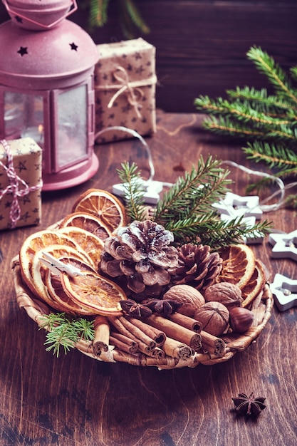 Naranja seca, anís estrellado, canela, piñas y abeto en placa rústica sobre mesa de madera. Idea de mezcla casera para el ambiente y el aroma navideños. Navidad ecológica con decoraciones naturales caseras.