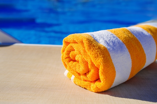 Foto naranja con toalla blanca sobre una tumbona de fondo de la piscina