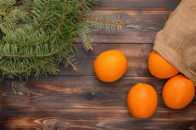 Naranjas en una bolsa de lino sobre una superficie de madera cerca de la vista superior de ramas de abeto